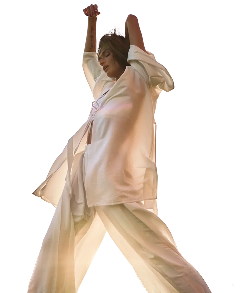 Person posing in flowing cream-colored outfit with arms raised against a neutral background